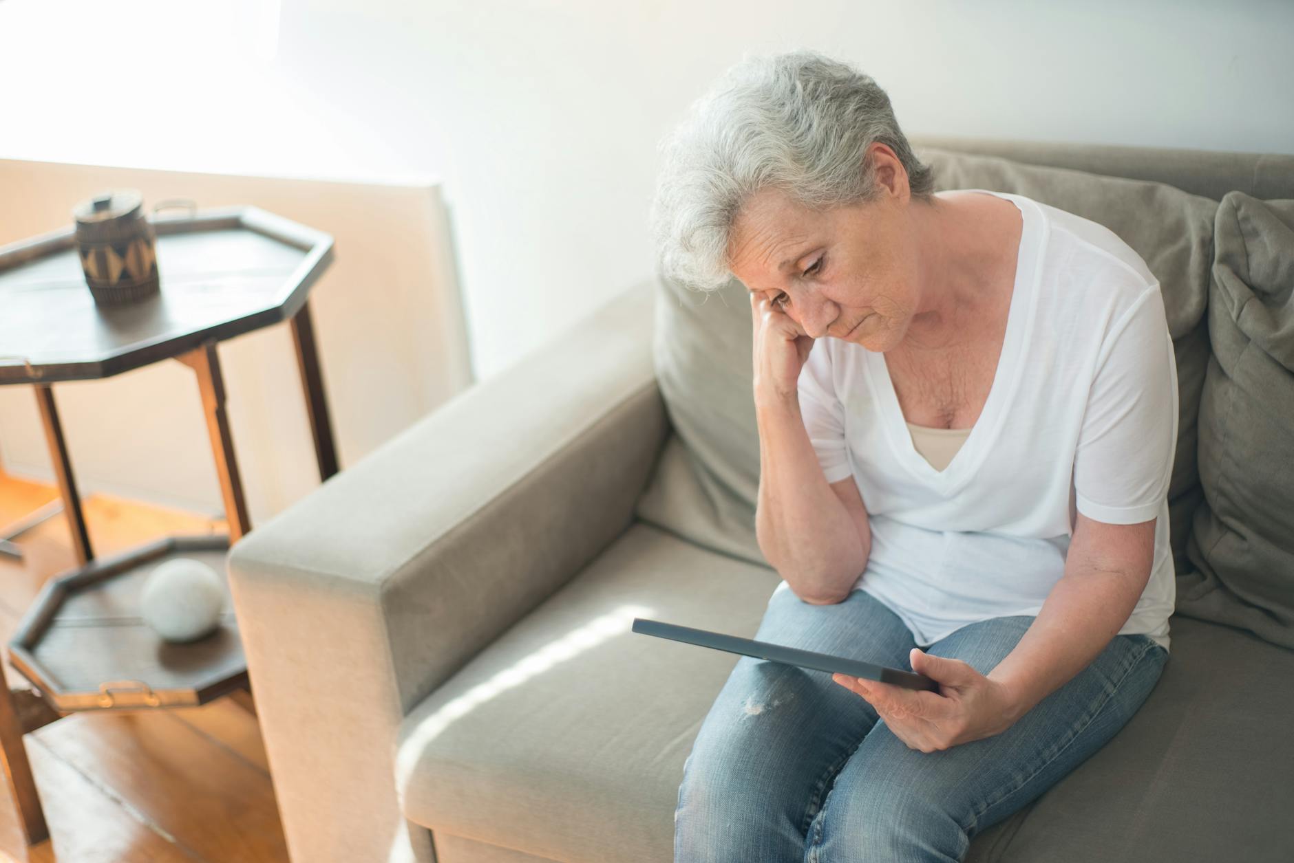 sad elderly woman sitting on a sofa while looking at a picture frame Why Empty Nesters Won’t Solve the Housing Crisis: Here’s What You Need to Know