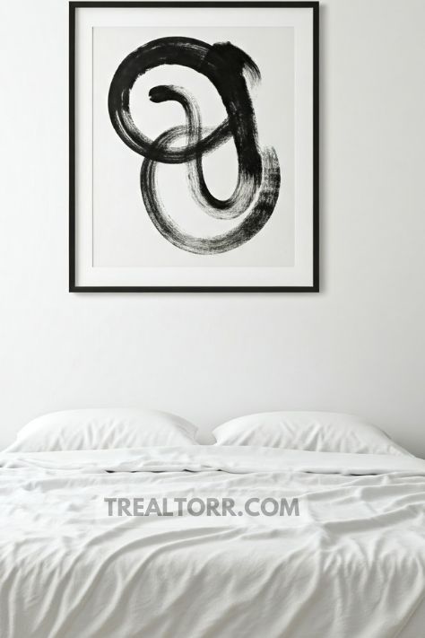A minimalist bedroom with a piece of abstract black-and-white wall art hanging above the bed.