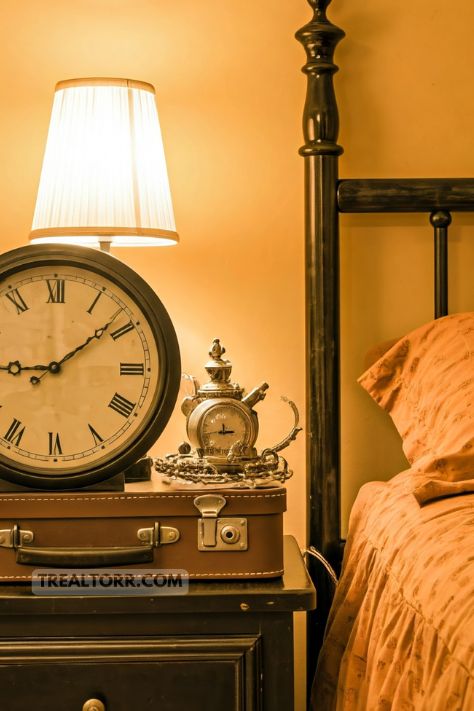 A vintage bedroom with charming accessories like an old clock with roman numerals, antique suitcases, and vintage trinkets scattered on a bedside table.